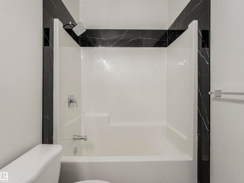 Bathtub and shower combination featuring a built-in seat, chrome fixtures, and dark marble-patterned tile accents - 36 Dalquist Bay, Leduc, AB 