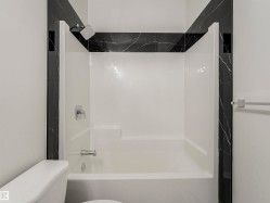 Bathtub and shower combination featuring a built-in seat, chrome fixtures, and dark marble-patterned tile accents - 