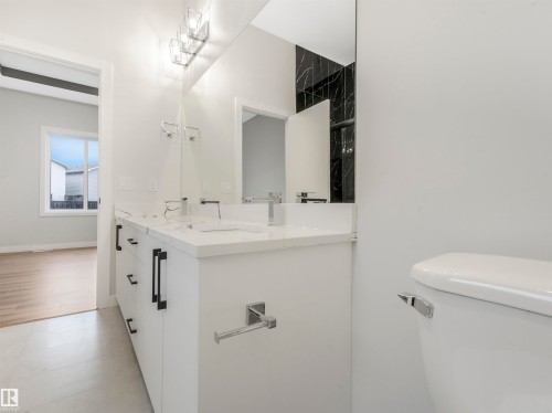 Dual vanity with integrated sinks, contemporary wall-mounted lighting, large frameless mirror, and black accent wall - 36 Dalquist Bay, Leduc, AB 