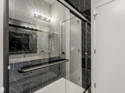 Frameless glass shower enclosure with black trim, black marble-look tile, and a white shower pan - 