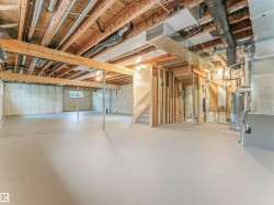 Spacious unfinished basement featuring exposed ceiling joists, structural support beams, a window, and utility hookups - 