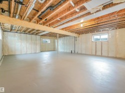 Expansive unfinished basement featuring a concrete floor, exposed wood ceiling joists, two windows, and insulated walls - 