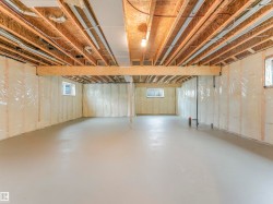 Unfinished lower level with exposed ceiling joists, concrete flooring, and multiple windows - 