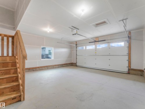Concrete flooring, light-toned walls, wooden staircase with railing, white garage door with upper windows, and a rectangular window - 36 Dalquist Bay, Leduc, AB 