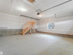 Unfinished garage with concrete flooring, exposed drywall, and a wood staircase - 