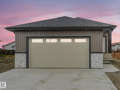 Contemporary exterior featuring vertical siding, stone veneer accents, and a panel garage door with upper lites - 36 Dalquist Bay, Leduc, AB 