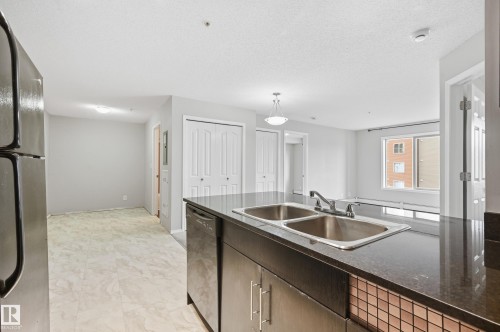 Kitchen island featuring a double basin stainless steel sink and dark countertop - #215 11804 22 Av Sw, Edmonton, AB 
