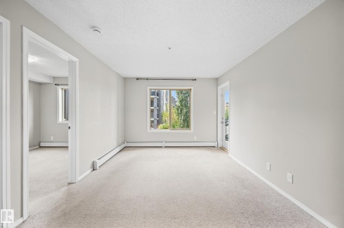 Spacious room featuring neutral carpeting, light-toned wall paint, and a window providing natural illumination - #215 11804 22 Av Sw, Edmonton, AB 