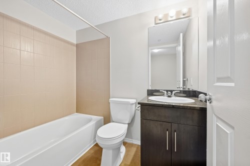 White bathtub with light-colored tile surround, toilet, and vanity with an integrated sink - #215 11804 22 Av Sw, Edmonton, AB 