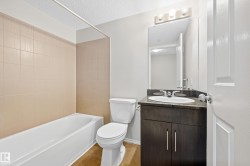 White bathtub with light-colored tile surround, toilet, and vanity with an integrated sink - 