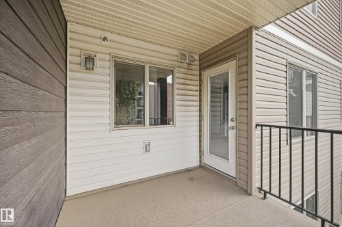 Exterior balcony with composite flooring, white vinyl siding, dark wood-finish siding accent, and black metal railing - #215 11804 22 Av Sw, Edmonton, AB 