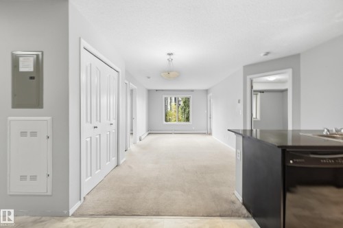 Open concept living area with light-colored carpeting, a kitchen island with a dark countertop, and a built-in dishwasher - #215 11804 22 Av Sw, Edmonton, AB 