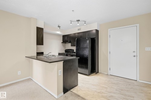 Kitchen featuring dark wood cabinetry, black appliances, a counter-height breakfast bar, track lighting, and tile flooring - #215 11804 22 Av Sw, Edmonton, AB 