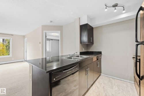Kitchen featuring dark cabinetry, dark countertops, a double stainless steel sink, a stainless steel dishwasher, and tiled flooring - #215 11804 22 Av Sw, Edmonton, AB 