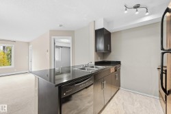 Kitchen featuring dark cabinetry, dark countertops, a double stainless steel sink, a stainless steel dishwasher, and tiled flooring - 