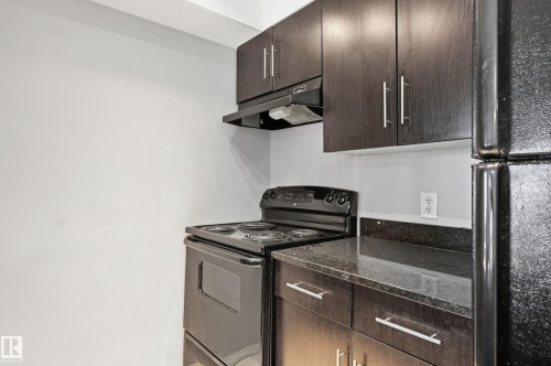 Dark wood-finish cabinetry, black electric range, black refrigerator, and dark countertops - #215 11804 22 Av Sw, Edmonton, AB 