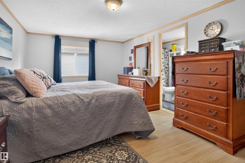 Wood-finish flooring with baseboard trim, window with blinds, overhead flush mount light, and a partially visible bathroom - 1405 53222 Range Road 272, Rural Parkland County, AB 