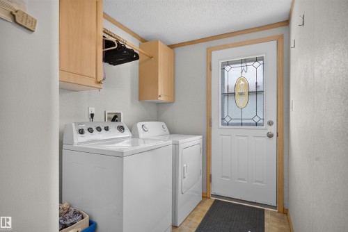Utility room featuring light wood-finish cabinetry, a built-in hanging rod, and a white entry door with decorative glass inserts - 1405 53222 Range Road 272, Rural Parkland County, AB 