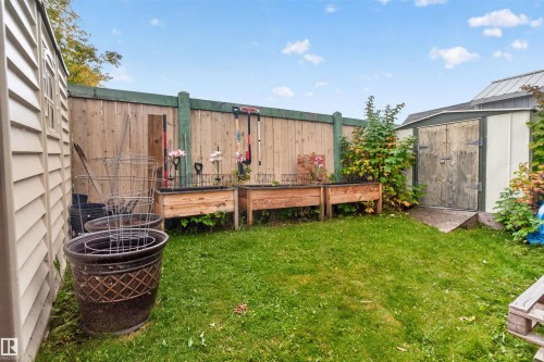 Fenced backyard featuring a storage shed, a second utility shed with horizontal siding, and two raised garden beds - 1405 53222 Range Road 272, Rural Parkland County, AB 