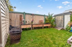 Fenced backyard featuring a storage shed, a second utility shed with horizontal siding, and two raised garden beds - 