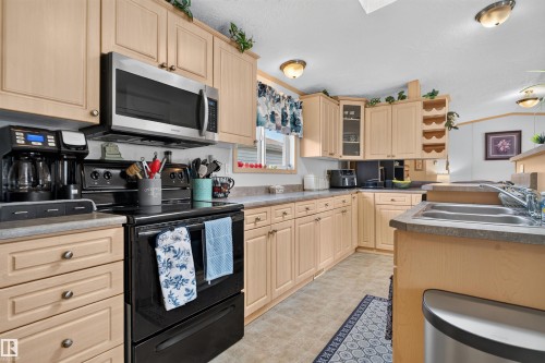 Kitchen featuring wood-finish cabinetry, stainless steel microwave, black electric range, dual basin sink, and a light-toned countertop - 1405 53222 Range Road 272, Rural Parkland County, AB 
