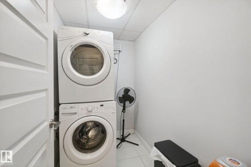 Stackable washer and dryer appliances, white paneled door, tile flooring, and overhead lighting - #125 5151 Windermere Bv Sw Sw, Edmonton, AB 