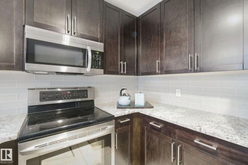 Wood-finish cabinetry paired with light-toned countertops, subway tile backsplash, and stainless steel appliances - #125 5151 Windermere Bv Sw Sw, Edmonton, AB 