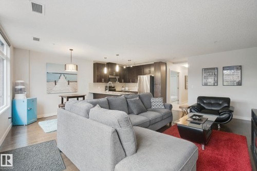 Open-concept living space with dark wood-finish flooring, recessed lighting, and large windows - #125 5151 Windermere Bv Sw Sw, Edmonton, AB 