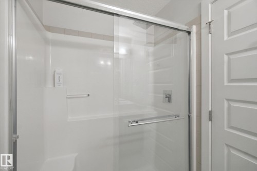 Sliding glass shower enclosure with a white acrylic surround, integrated shelving, and a polished chrome shower fixture - #125 5151 Windermere Bv Sw Sw, Edmonton, AB 