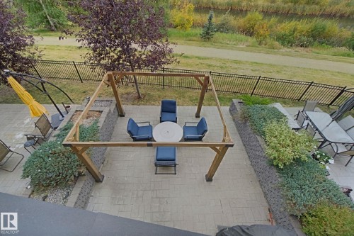 Expansive paver patio with a wooden pergola structure, surrounded by tiered landscaping featuring retaining walls, mature shrubs, and a wrought iron fence - #125 5151 Windermere Bv Sw Sw, Edmonton, AB 