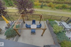 Expansive paver patio with a wooden pergola structure, surrounded by tiered landscaping featuring retaining walls, mature shrubs, and a wrought iron fence - 