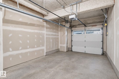 Garage space featuring a concrete floor, exposed ceiling, and an overhead garage door with upper window panels - #125 5151 Windermere Bv Sw Sw, Edmonton, AB 