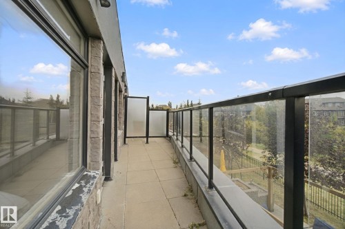 Expansive balcony featuring a tiled surface, stone-clad exterior wall, large windows, and a glass-paneled railing - #125 5151 Windermere Bv Sw Sw, Edmonton, AB 