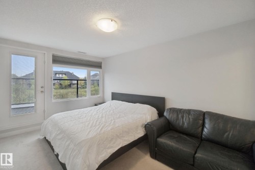 White walls with overhead flush-mount lighting, large window with roller shade, and light-toned carpet flooring - #125 5151 Windermere Bv Sw Sw, Edmonton, AB 