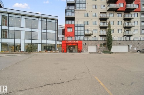 Modern multi-story building featuring extensive glazing, private balconies with glass railings, a prominent red-paneled entrance, and integrated ground-level garage doors - #125 5151 Windermere Bv Sw Sw, Edmonton, AB 