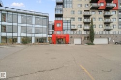 Modern multi-story building featuring extensive glazing, private balconies with glass railings, a prominent red-paneled entrance, and integrated ground-level garage doors - 