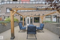Paved outdoor patio featuring a wooden pergola, raised planting beds with retaining walls, and a stone facade - 