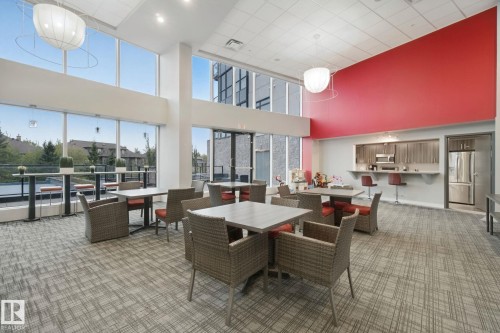 Spacious common area featuring floor-to-ceiling windows, high ceilings, and a built-in kitchen bar with wood-finish cabinetry and stainless steel appliances - #125 5151 Windermere Bv Sw Sw, Edmonton, AB 