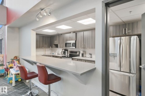 Kitchenette featuring a pass-through counter, stainless steel appliances, recessed ceiling lights, track lighting, and wood-finish cabinetry - #125 5151 Windermere Bv Sw Sw, Edmonton, AB 