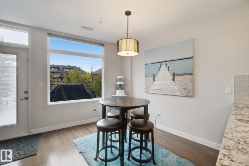 Large window offering natural light, wood-finish flooring, white walls, pendant light fixture, and light-toned countertop - #125 5151 Windermere Bv Sw Sw, Edmonton, AB 