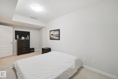 Carpeted flooring with white baseboards, a white paneled door, and a flush-mount ceiling light fixture - #125 5151 Windermere Bv Sw Sw, Edmonton, AB 