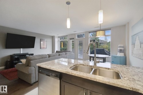Kitchen island with a double basin stainless steel sink, granite countertop, and integrated dishwasher - #125 5151 Windermere Bv Sw Sw, Edmonton, AB 