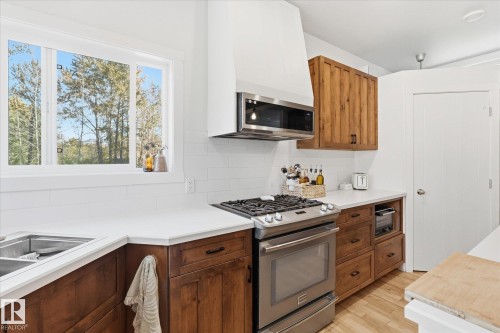 Stainless steel range with a coordinating microwave, white subway tile backsplash, wood-finish cabinetry, white countertops, and a double basin sink - #45 53122 Rge Road 14, Rural Parkland County, AB 