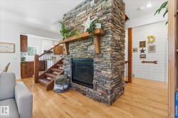 Stone-clad fireplace with wood mantel, hardwood flooring, and wood stairway with metal balusters - 