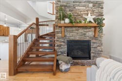 Wood staircase with black metal balusters, stacked stone fireplace, wood mantel, and light wood-finish flooring - 