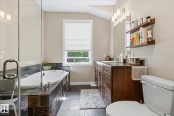 Full-size bathtub with a tile surround, glass-enclosed shower, dual-sink vanity with wood-finish cabinetry, and neutral wall tones - 