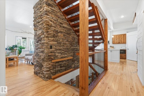 Stone accent wall, wood-finish flooring, open-tread staircase with wood newel posts, black metal balusters, and white cabinetry with wood-finish upper cabinets - #45 53122 Rge Road 14, Rural Parkland County, AB 