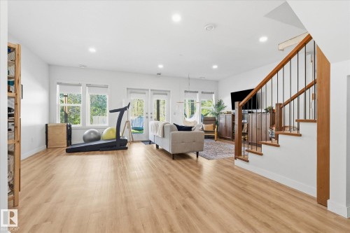 Wood-finish flooring throughout, white walls, recessed ceiling lights, multiple windows, and a staircase with a wood handrail and black metal balusters - #45 53122 Rge Road 14, Rural Parkland County, AB 