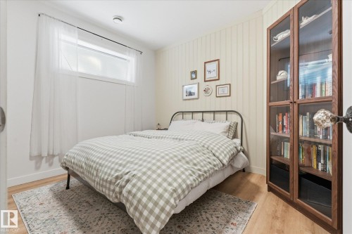Bright secondary bedroom featuring a metal bed frame, plaid bedding, wood-finish flooring, and soft natural light from a transom window - #45 53122 Rge Road 14, Rural Parkland County, AB 