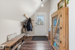 Vaulted ceiling entryway with wood-finish flooring, white paneled door with glass insert, and built-in wood shelving - 